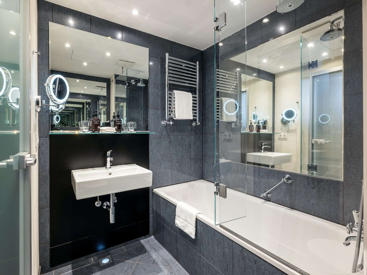 Ein grau gefliestes Badezimmer mit Waschbecken, Badewanne und einem großen Spiegel