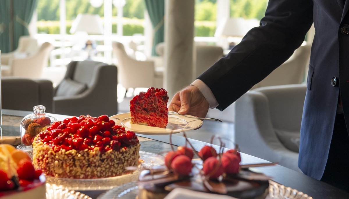 A man in a suit serves a piece of strawberry cake, on the table is a whole layered strawberry cake