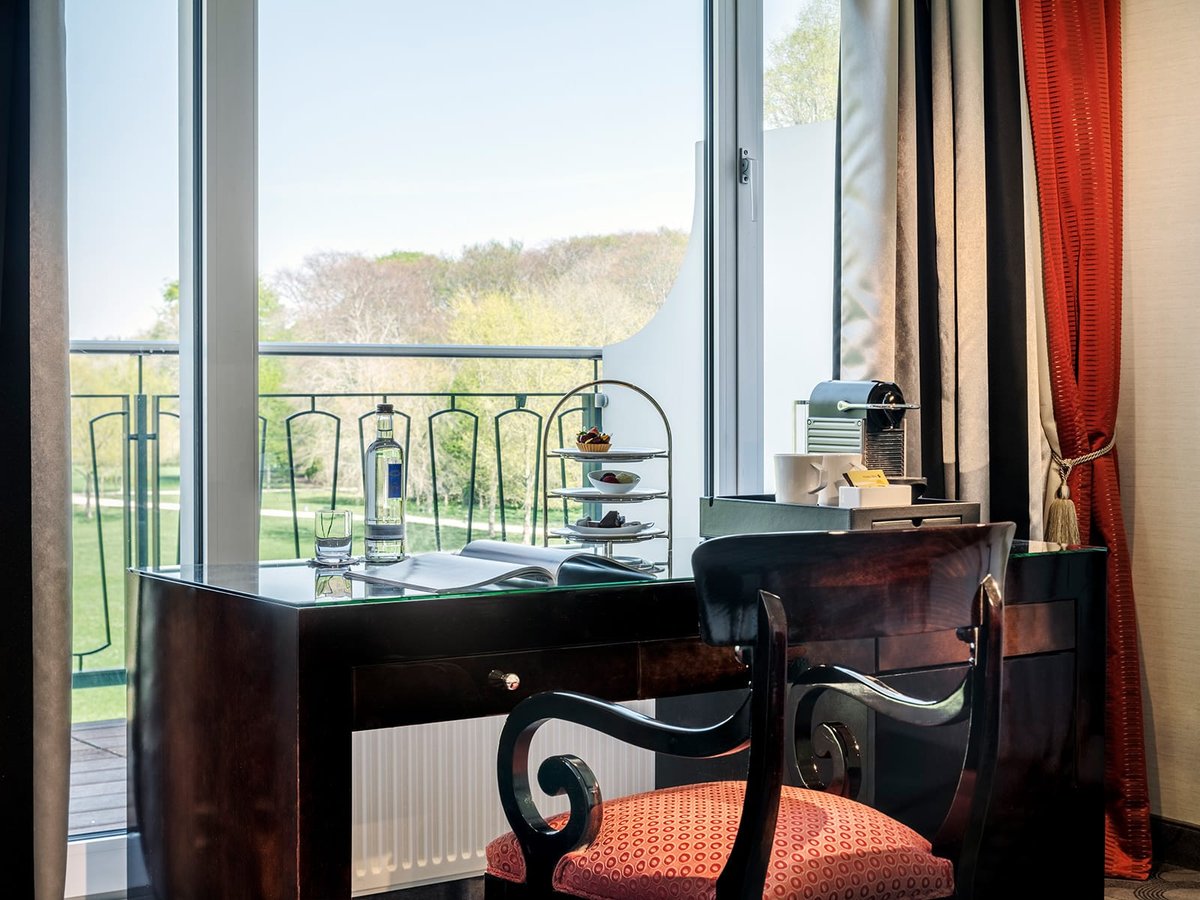 Ein Schreibtisch mit Glasplatte, Kaffee und Pralinen einer Suite des Parkhotels Bremen mit Ausblick auf einen See