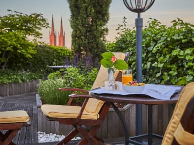 Kleiner Tisch mit einer Schale voller Früchten und frischem Saft auf einer Terrasse voller Pflanzen mit schönen Ausblick
