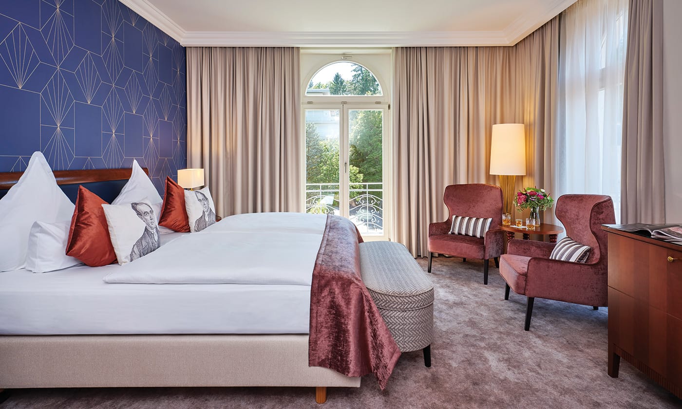 Hell eingerichtetes Superior Zimmer für ein Wellness-Wochenende in Baden Baden mit blauer Tapete und gemütlichem Doppelbett