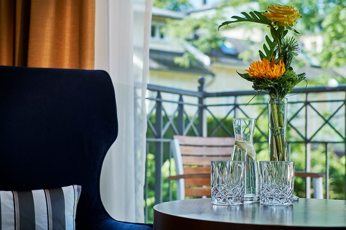 Tisch mit Karaffe, zwei Gläsern und Blumenvase mit sommerlichen Blumen im Standard Zimmer des Luxushotels Maison Messmer in Baden Baden