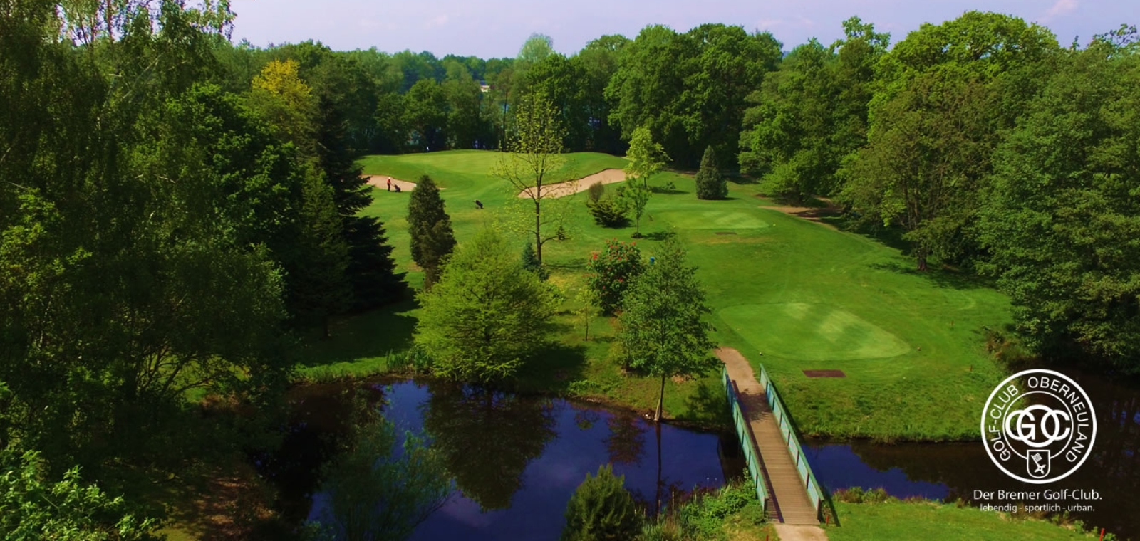 Blick von oben auf den grünen Golfplatz nahe des Hommage Hotels mit einem durchquerenden Fluss