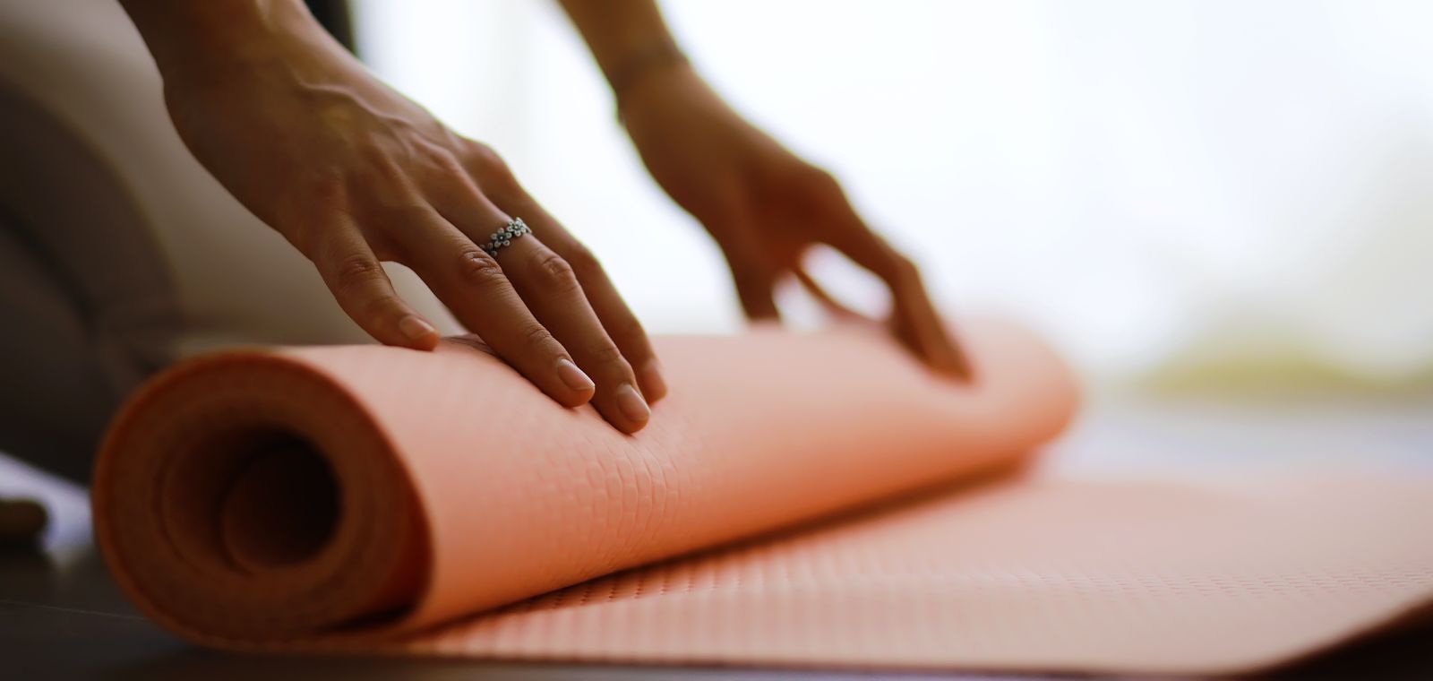 Nahaufnahme einer Frau, wie sie eine orangene Yoga-Matte ausrollt