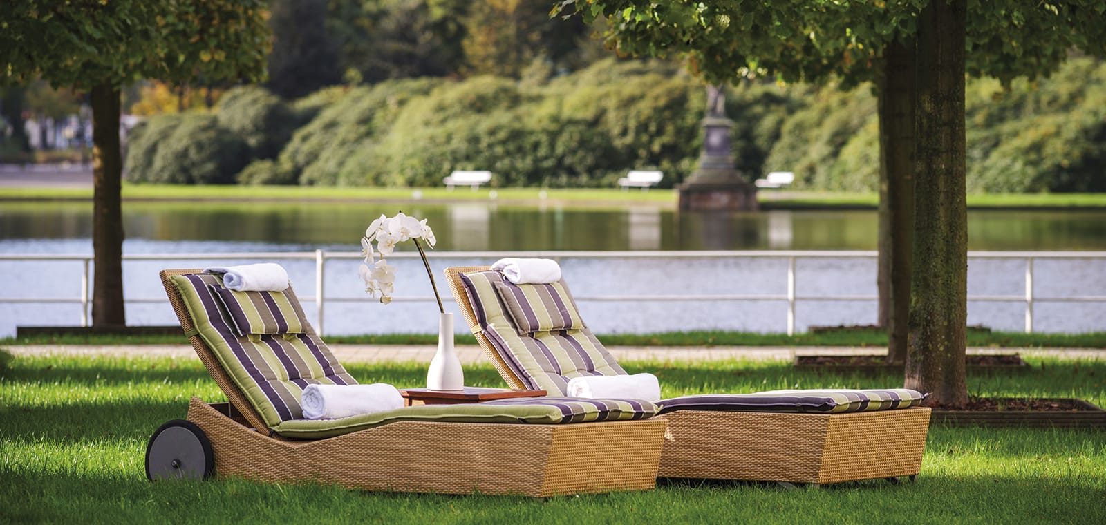 Zwei Relaxliegen im Bürgerpark beim Wellnesshotel Bremen mit weißen Orchideen und dem See im Hintergrund im Wellnesshotel Bremen