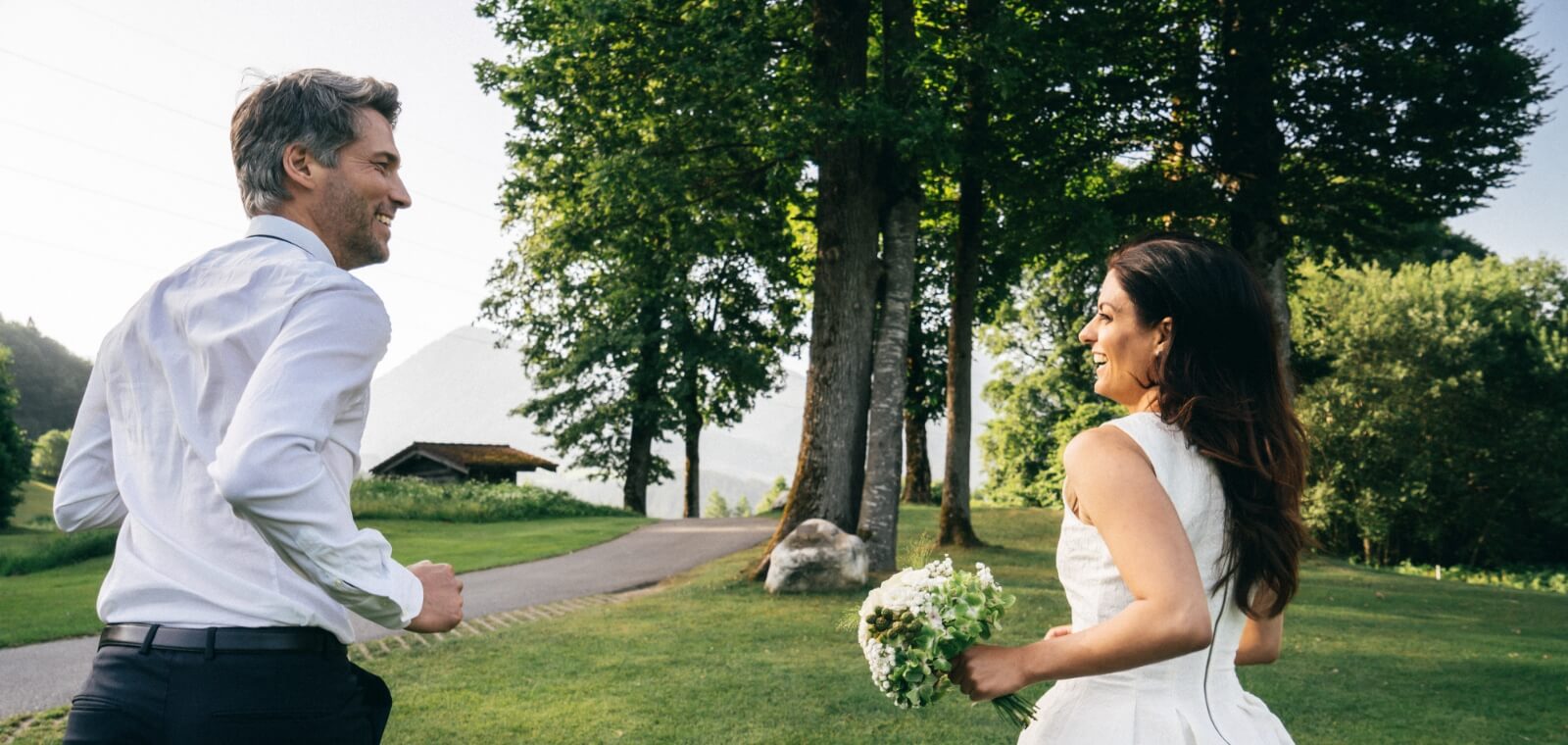 A happy couple on a lawn with trees on their wedding venue in Austria